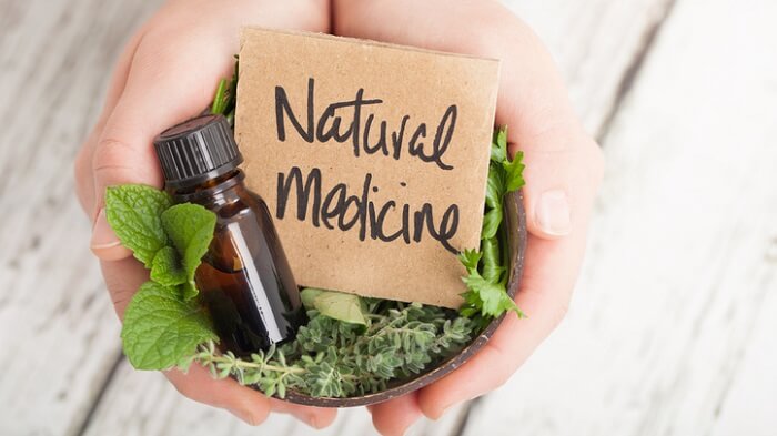 Bowl of herbs and essential oil and card saying Natural Medicine on light floor boards