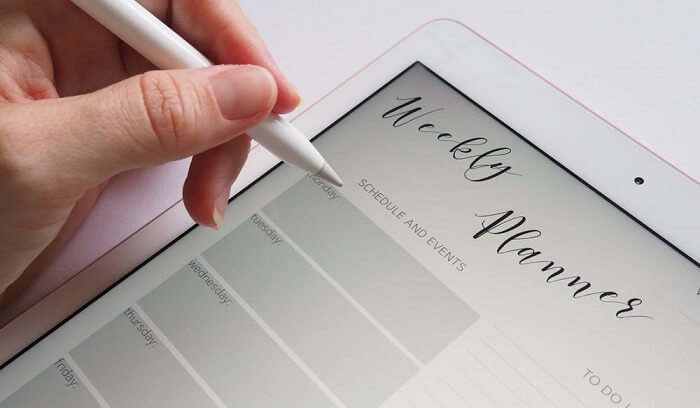 woman writing in weekly planner on tablet