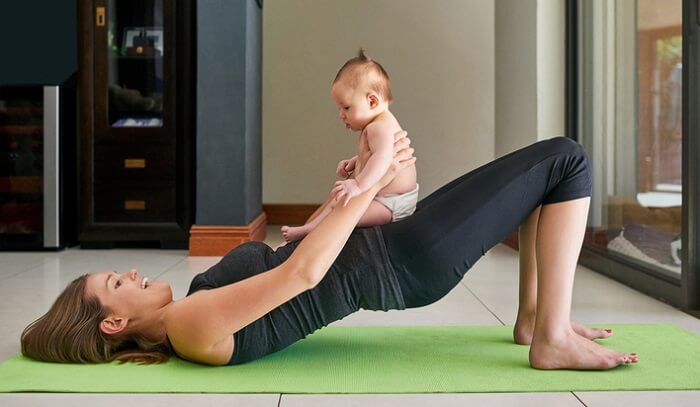 young mother doing yoga mat exercise with baby on her stomach