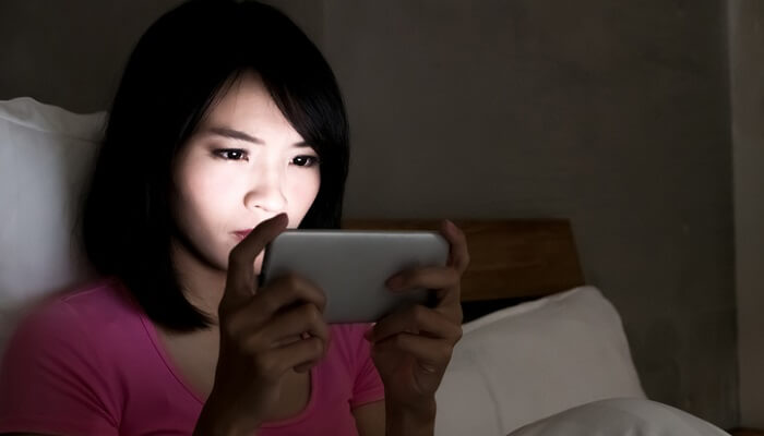 young woman looking at cell phone in bed