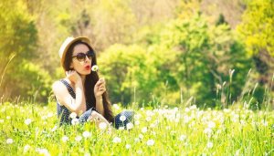 immune system allergies concept - young woman in field blowing on dandelion