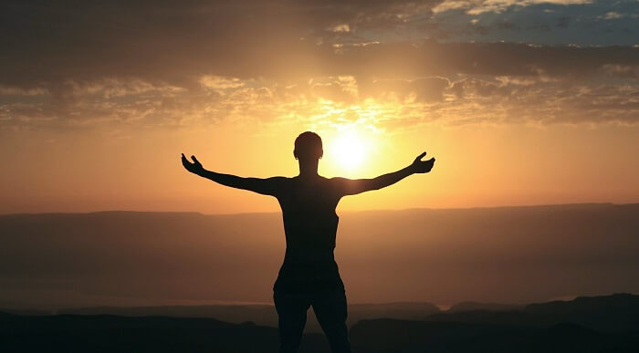 man with arms open towards setting sun