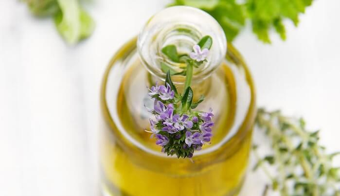 thyme leaves and flowers next to clear essential oil bottle