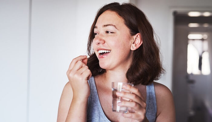 happy young woman taking supplement pill