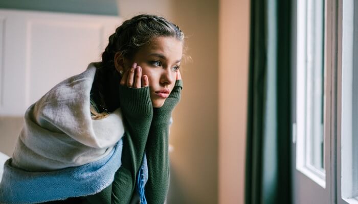 young depressed woman sitting on bed looking out window