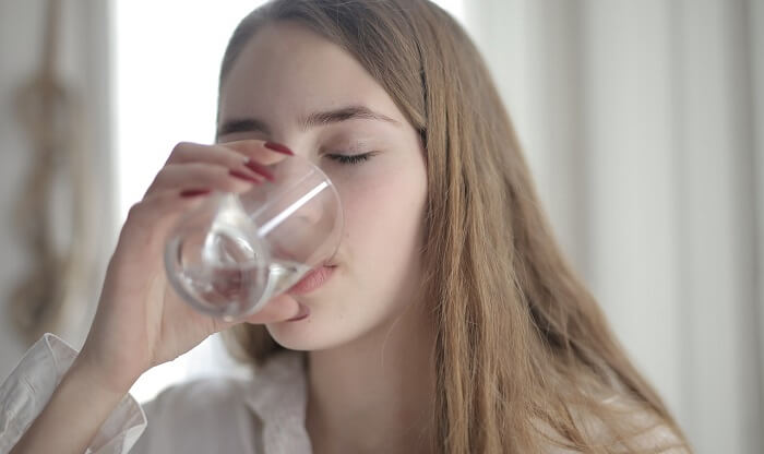 giovane che beve acqua da un bicchiere