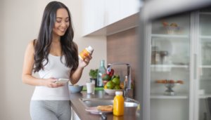 smiling young woman in kitchen looking at supplement bottle