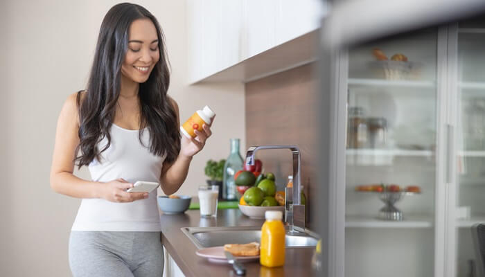 smiling young woman in kitchen looking at supplement bottle