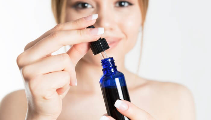 young woman opening dropper bottle - essential oils for wrinkles concept