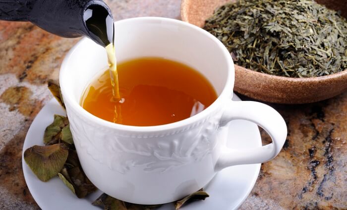 cup of greeen tea next to bowl of tea leaves