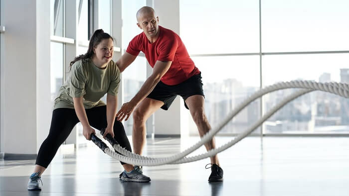 trainer with young girl getting movement with battle ropes