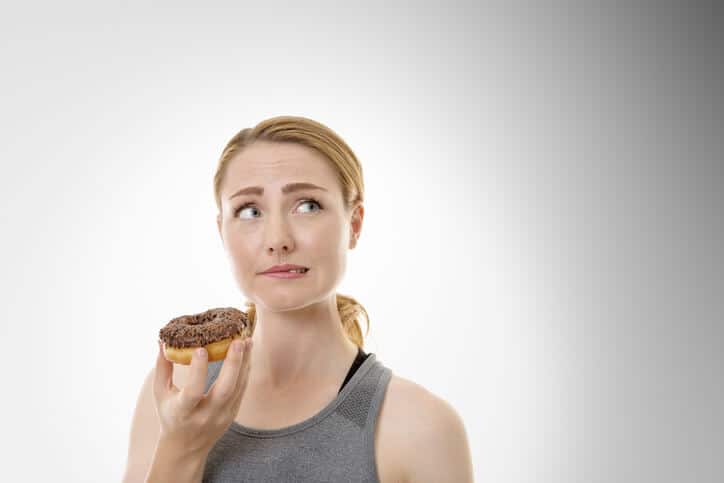 young woman with donut in hand feeling guilty