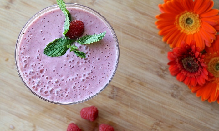 berry smoothie next to berries and flowers on table