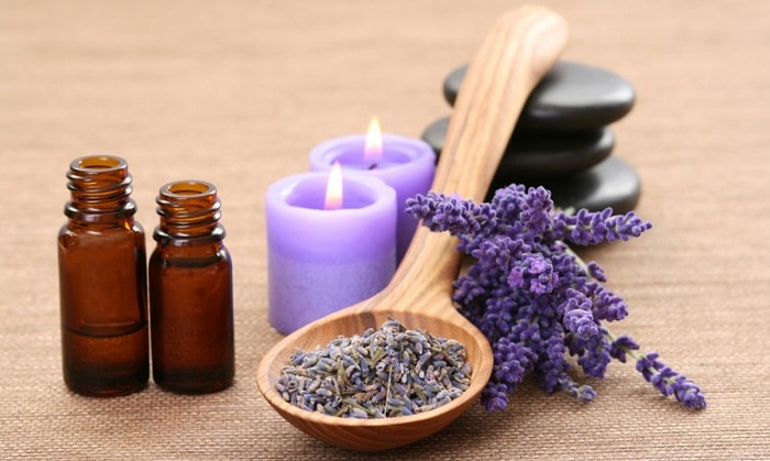 lavender herbs in wooden spoon and flowers next to candles and essential oils
