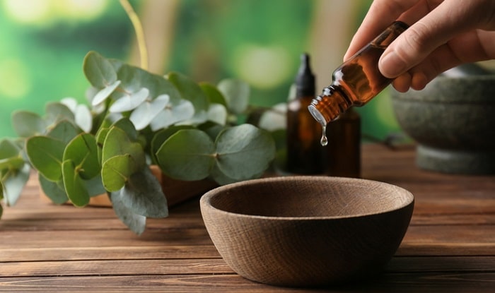 eucalyptus leaves next to oil being poured into bowl