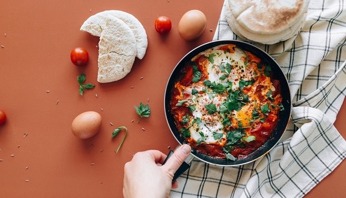 baked shakshuka next to eggs and tomatoes and pita bread