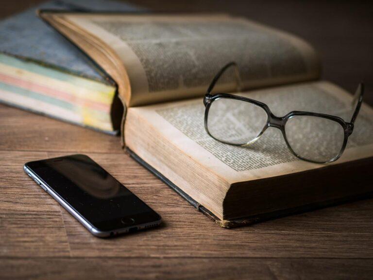 cell phone next to open book with glasses on it