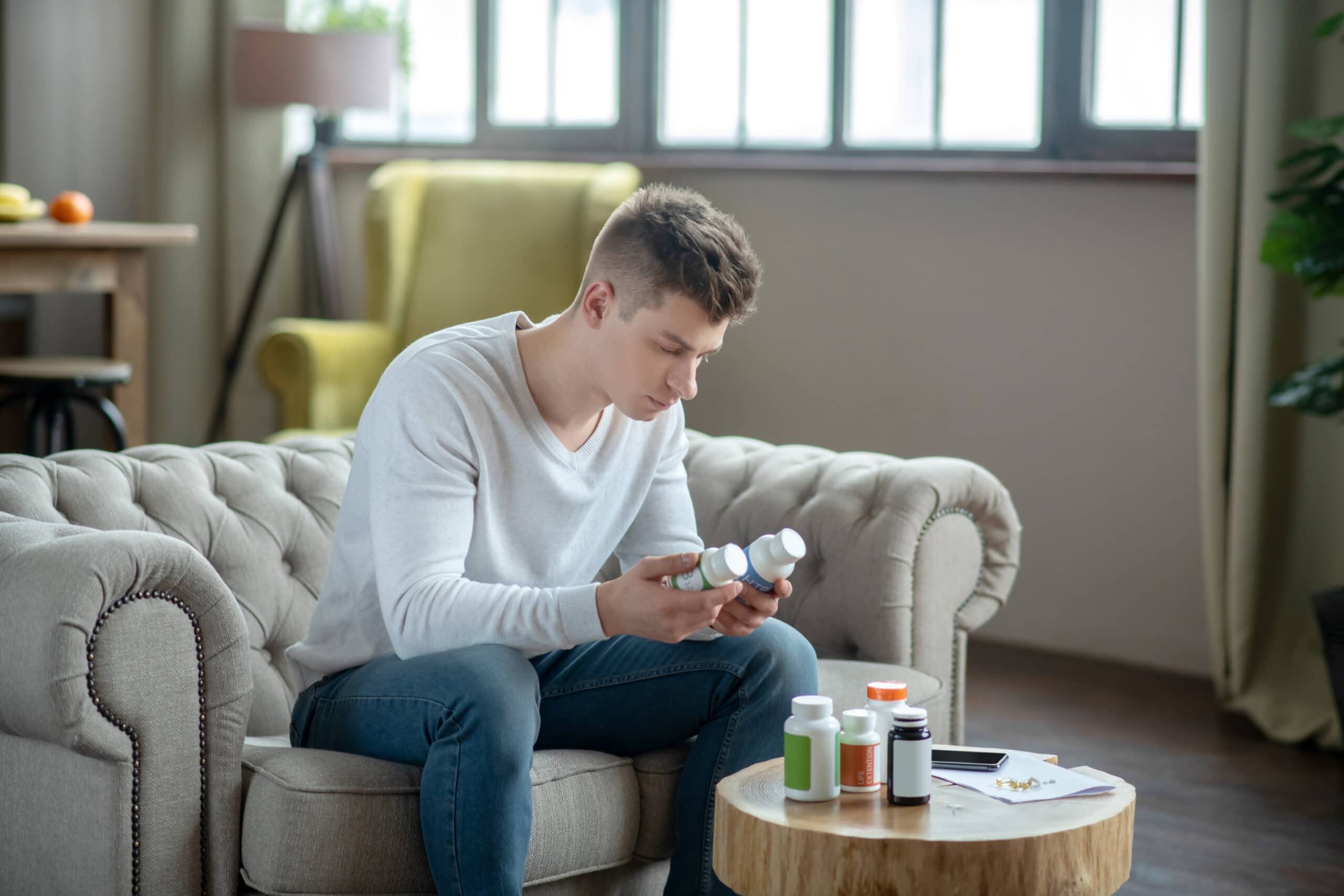 young man looking at supplement labels next to various supplements on table