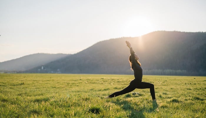 Young woman practicing yoga in grassy meadow at sunrise