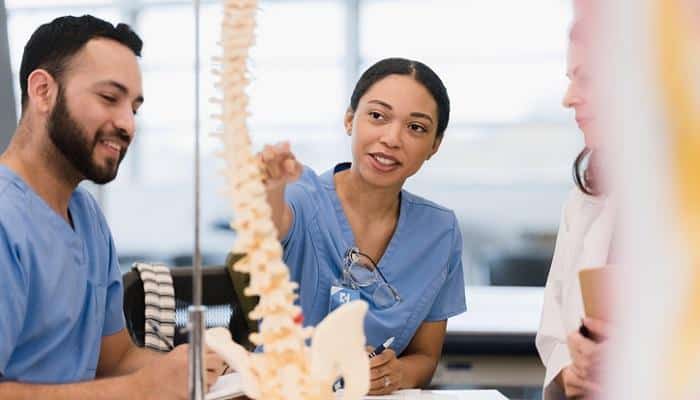 medical school students studying model of vertebrae