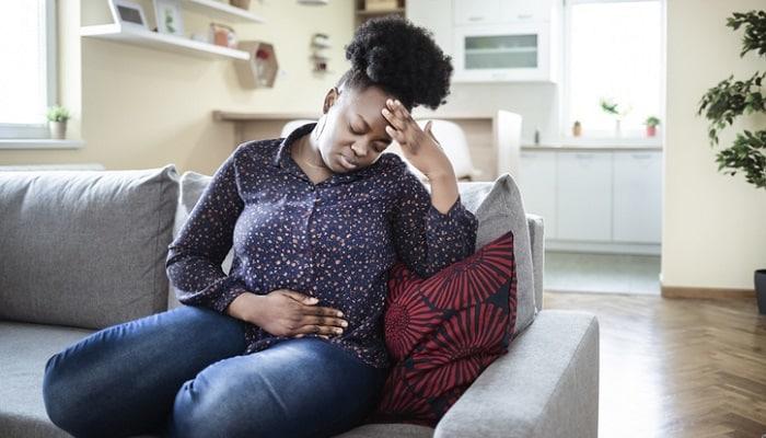 Woman holding stomach while sitting on a couch
