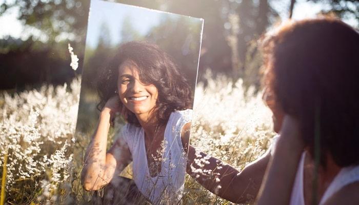 happy young woman looking at mirror in field