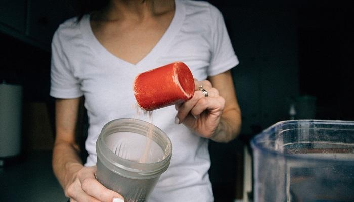 woman pouring protein powder into bottle