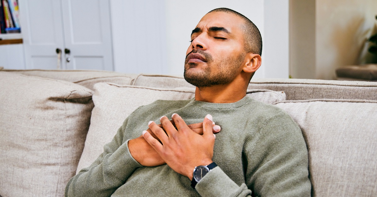 man sitting on couch holding his heart