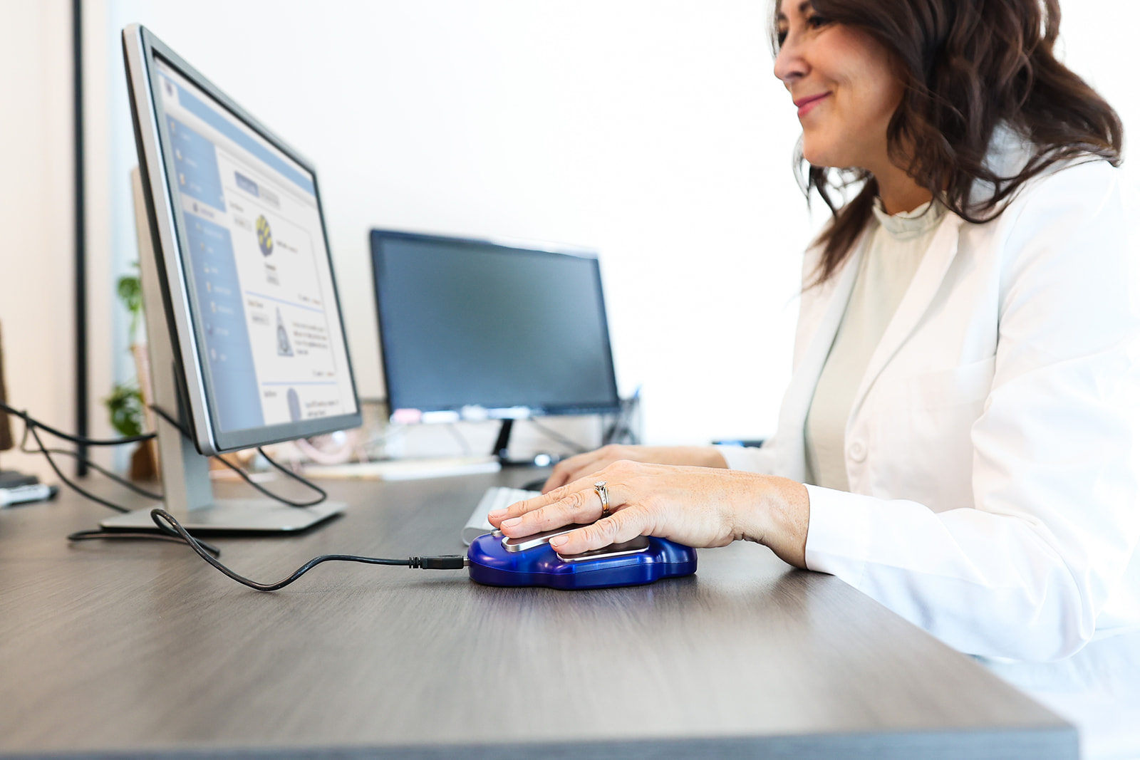 Practitioner sitting at a desk using a computer with her hand on a ZYTO hand cradle